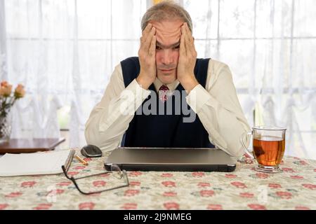 Uomo maturo che lavora su un notebook a casa con una cravatta e un giubbotto Foto Stock
