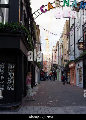 Londra, Greater London, Inghilterra, maggio 11 2022: Donna al telefono a Carnaby Street con il cartello stradale sopra e gru dietro. Foto Stock