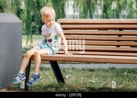 Giochi per bambini piccoli nel parco, salite sulla panca. Il bambino è seduto su una panca del parco. Foto Stock