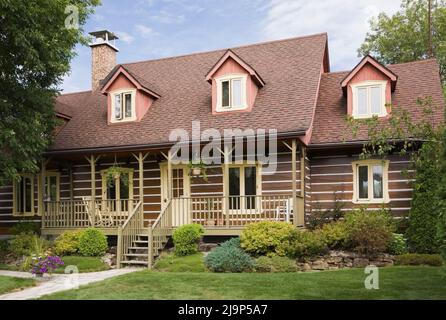 Replica del vecchio 1800s Canadiana casa in stile casolare di tronchi con giardino paesaggistico davanti in estate. Foto Stock