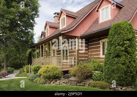 Replica del vecchio 1800s Canadiana casa in stile casolare di tronchi con giardino paesaggistico davanti in estate. Foto Stock