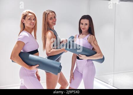 Ritratto di donne attive sorridenti in abbigliamento sportivo con tappetini yoga prima di allenarsi in palestra Foto Stock