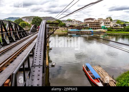 I turisti camminano attraverso il famoso ponte sul fiume Kwai e un motoscafo siede ad un molo sotto il ponte. Foto Stock