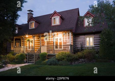 Replica del vecchio casolare 1800s Canadiana casa di tronchi con giardino paesaggistico davanti in estate al tramonto. Foto Stock