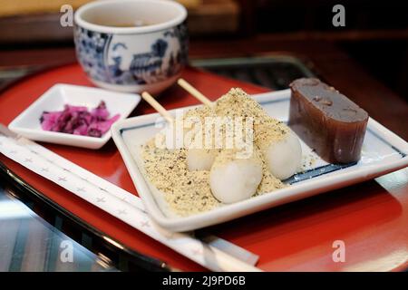 Un piatto di dolci tradizionali giapponesi - gelatina di fagioli rossi e palle di torta di riso con polvere di fagioli - servito con una tazza di hojicha Foto Stock