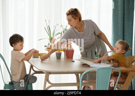 Famiglia con bambini divertirsi a casa al tavolo, creando arte fatta a mano. Madre e bambini disegnare e comunicare in cucina, emotivo Foto Stock
