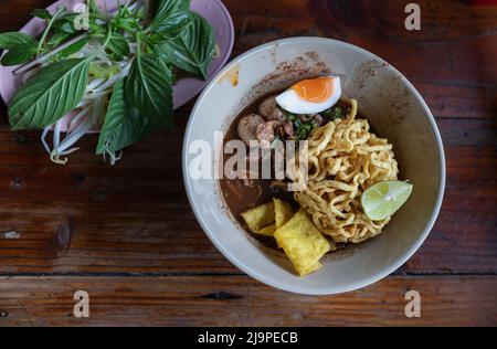 Tagliatelle croccanti di uova gialle fritte in zuppa addensata aggiunta di sangue con palle di maiale, maiale affettato, uova di bael affettato, lime affettato e wonton croccante (uova di tok di Nam Foto Stock