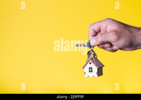 Acquisto di una casa. L'acquirente riceve la chiave per la proprietà. Appartamento ipotecario. Chiavi e una piccola casa in legno in mano. Consegna delle chiavi all'Ora Foto Stock