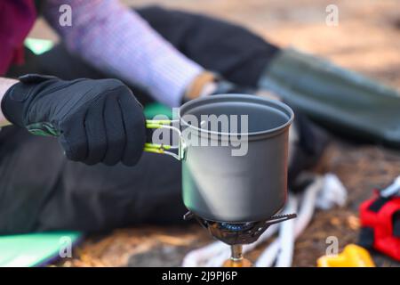 Cibo da cucina turistico maschile su bruciatore a gas portatile in foresta, primo piano Foto Stock