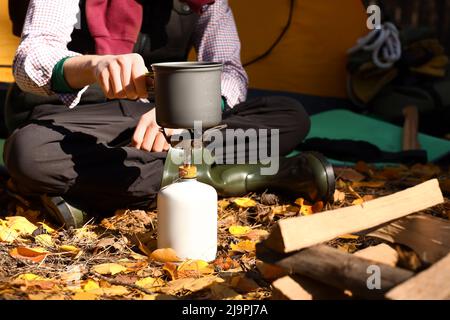 Cibo da cucina turistico maschile su bruciatore a gas portatile in foresta Foto Stock