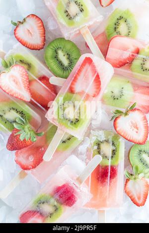 Vista dall'alto in basso di un mucchio di fresche fragole kiwi popsicles su ghiaccio. Foto Stock