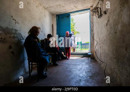 Una donna anziana seduta accanto a due bambini all'ingresso del bunker dove partono nella periferia della città. Lysychansík, regione di Luhansk. 23 maggio 2022 Lysychansk è una città allungata sulla riva destra del fiume Donets nella regione di Luhansk. La città fa parte di un'area metropolitana che comprende Severodonetsk e Rubizhne; le tre città insieme costituiscono uno dei più grandi complessi chimici dell'Ucraina. La città si trova a circa 7 km dalla prima linea, e le truppe russe si stanno muovendo verso di essa, la città, come Severodonetsk, è quasi isolata. I russi stanno cercando di occupare la strada principale t Foto Stock