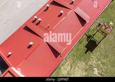 tetto in metallo corrugato rosso con tubi installati di sistemi di ventilazione. vista aerea dall'alto. Foto Stock