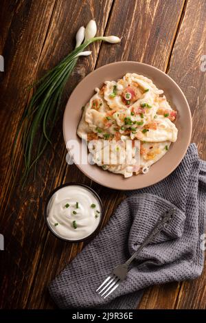 Gnocchi di patate con panna acida sul tavolo di legno. Cibo tradizionale ucraino. Varenyky, vareniki, pierogi, pirohi - gnocchi con ripieno. Foto Stock