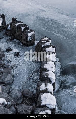 Vecchi pali di legno con calotte di neve in fiume ghiacciato all'alba fredda stagione invernale. Foto Stock