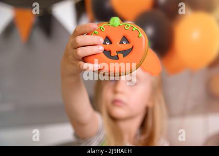 primo piano di un biscotto che assomiglia ad una zucca nella mano di una bambina Foto Stock