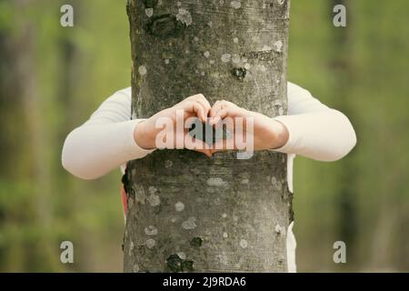 Le mani del bambino che fanno una forma del cuore su un tronco dell'albero. Abbracciare, proteggere il concetto di natura. Foto Stock