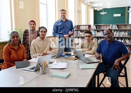 Ritratto di gruppo di insegnanti di lingua inglese moderna e studenti immigrati multietnici che hanno classe in biblioteca guardando la macchina fotografica Foto Stock