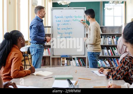 Gruppo di studenti immigrati moderni che imparano verbi irregolari di lingua inglese a scuola Foto Stock