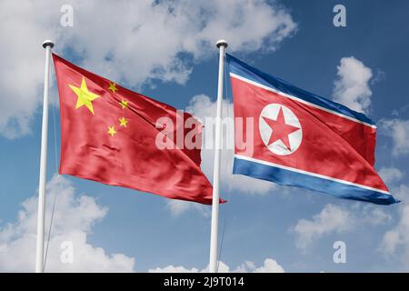 Cina e Corea del Nord due bandiere su flagpoli e sfondo blu cielo nuvoloso Foto Stock