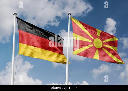 Germania e Macedonia del Nord due bandiere su flagpoli e sfondo blu cielo nuvoloso Foto Stock