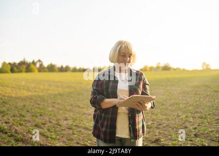 Fermer donna agronomista che ispeziona le colture di soia che crescono nel campo agricolo. Agricoltura, giardinaggio, business o concetto di ecologia. Foto Stock