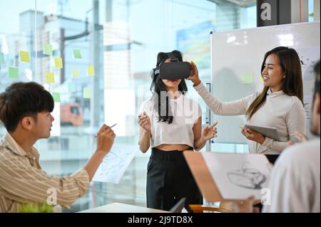 Un team di start-up di aziende tecnologiche che ha una riunione per discutere e discutere del loro nuovo progetto di realtà virtuale. Donna che indossa occhiali VR durante la riunione. Foto Stock