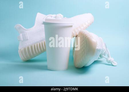 Sneaker bianche e una tazza di carta bianca con caffè Foto Stock