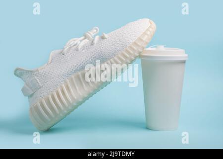 Sneaker bianche e una tazza di carta bianca con caffè Foto Stock