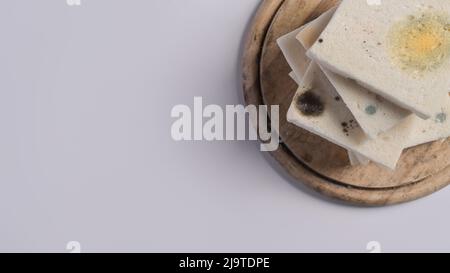 Muffa che cresce rapidamente su pane ammuffito in spore verdi e bianche su tagliere di legno. Foto Stock