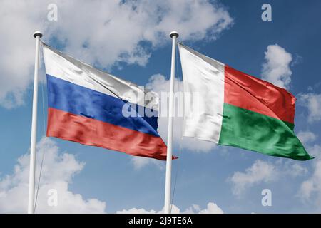 Russia e Madagascar due bandiere su flagpoli e sfondo blu cielo nuvoloso Foto Stock