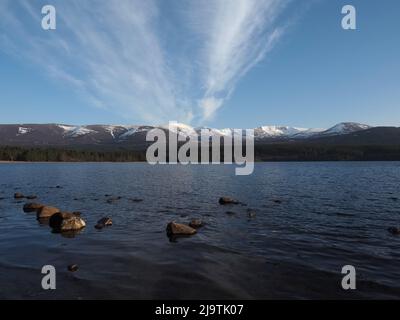 Vista da Loch Morlich, di Cairn Gorm e del Northern Corries con una neve coperta. In tarda serata di primavera, con nuvole di cirro contro un cielo blu. Foto Stock