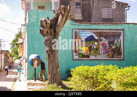La gente cubana occasionale è vista da un piccolo parco nella via Colon. Un uomo parla su un telefono a pagamento Etecosa. Una pittura di mattonella o arte decora il laterale Foto Stock