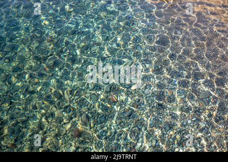 Trama di acque blu turchesi trasparenti che ondulano il mare con piccole pietre sotto la superficie Foto Stock
