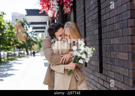 donna gioiosa che tiene bouquet di fiori di eustoma mentre il ragazzo che la abbraccia per strada Foto Stock