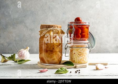 Pomodori sottaceto, kimchi, cavolo in vaso con aglio, pepe e foglie di alloro su tavola bianca di legno con fondo grigio Foto Stock