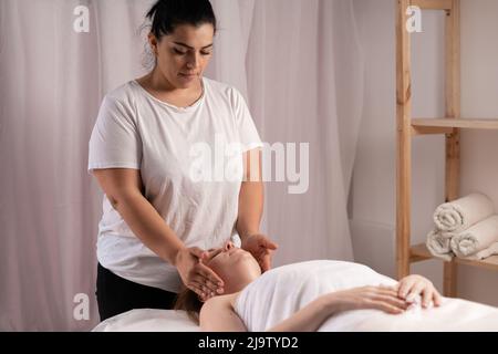 Giovane donna con massaggio nel salone termale, massaggio boccale facciale con scolpitura manuale. Massaggio viso ringiovanente in cosmetologia Foto Stock