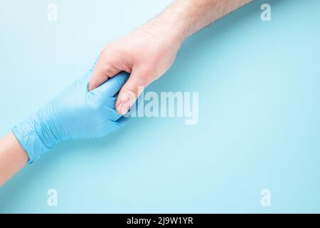 Concetto di tocco proibito tra la mano del female in guanto medico e la mano dell'uomo su sfondo blu. Concetto di protezione. Foto Stock