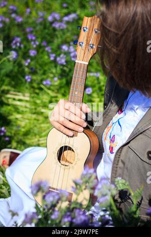 Ukulele strumento musicale in mano femminile. Donna seduta in fiori in primavera Foto Stock