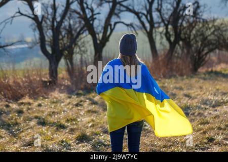 Donna coperta da bandiera ucraina in piedi sul campo. Concetto di speranza e libertà per il paese ucraino Foto Stock