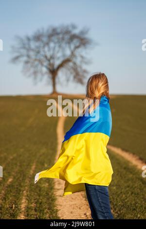 Donna coperta da bandiera ucraina in piedi sul campo. Concetto di speranza e libertà per il paese ucraino Foto Stock