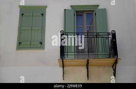 Vecchia facciata neoclassica casa con persiane in legno verde oliva e un balcone con ringhiera in ferro battuto artigianale su una parete bianca. Foto Stock