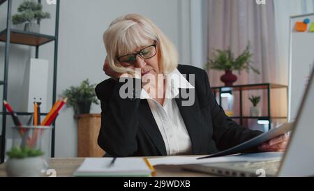 Stanco, addormentata, donna anziana che lavora in modo stressato e addormentata, si siede alla scrivania dell'ufficio domestico con un computer portatile Foto Stock