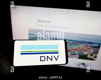 Persona che tiene uno smartphone con il logo della società di servizi norvegese DNV SULLO schermo di fronte al sito Web. Mettere a fuoco sul display del telefono. Foto Stock