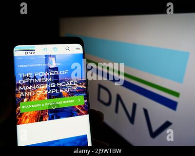 Persona che detiene il cellulare con il sito web della società di servizi norvegese DNV COME sullo schermo di fronte al logo aziendale. Concentrarsi sul centro del display del telefono. Foto Stock