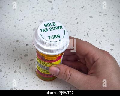 Seattle, WA USA - circa Maggio 2022: Vista dall'alto in basso di una mano che tiene una bottiglia di pillola di prescrizione su un piano bianco. Foto Stock