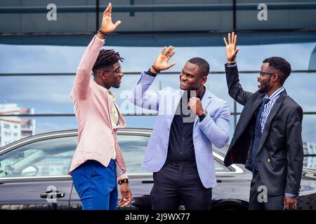 Un gruppo dei loro tre uomini d'affari africani americani di successo in un abito elegante che parla e gioisce sulla strada grattacielo finestra sfondo Foto Stock