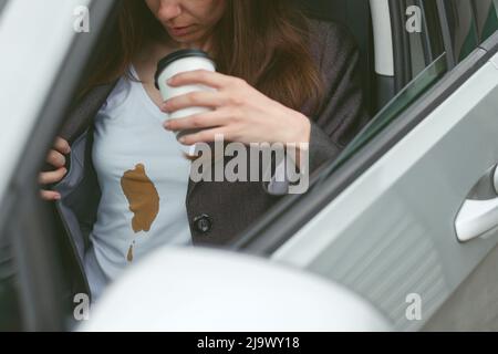 La donna di affari ha versato il caffè sulla camicia dietro il volante di un'automobile. Concetto di pulizia delle macchie sui vestiti Foto Stock
