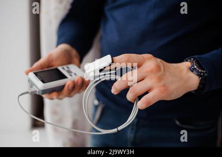 Uomo che utilizza il pulsossimetro a dito, concetto di monitoraggio sanitario. Pulsossimetro su sfondo Foto Stock