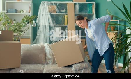 La donna sente dolore improvviso alla schiena quando si tenta di sollevare una scatola di cartone. Foto Stock